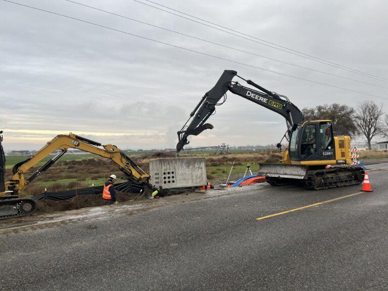 Excavators placing a fiber vault beside the road